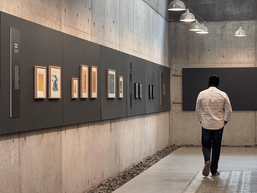 A back shot of a person walking in an art gallery with several artworks on display.