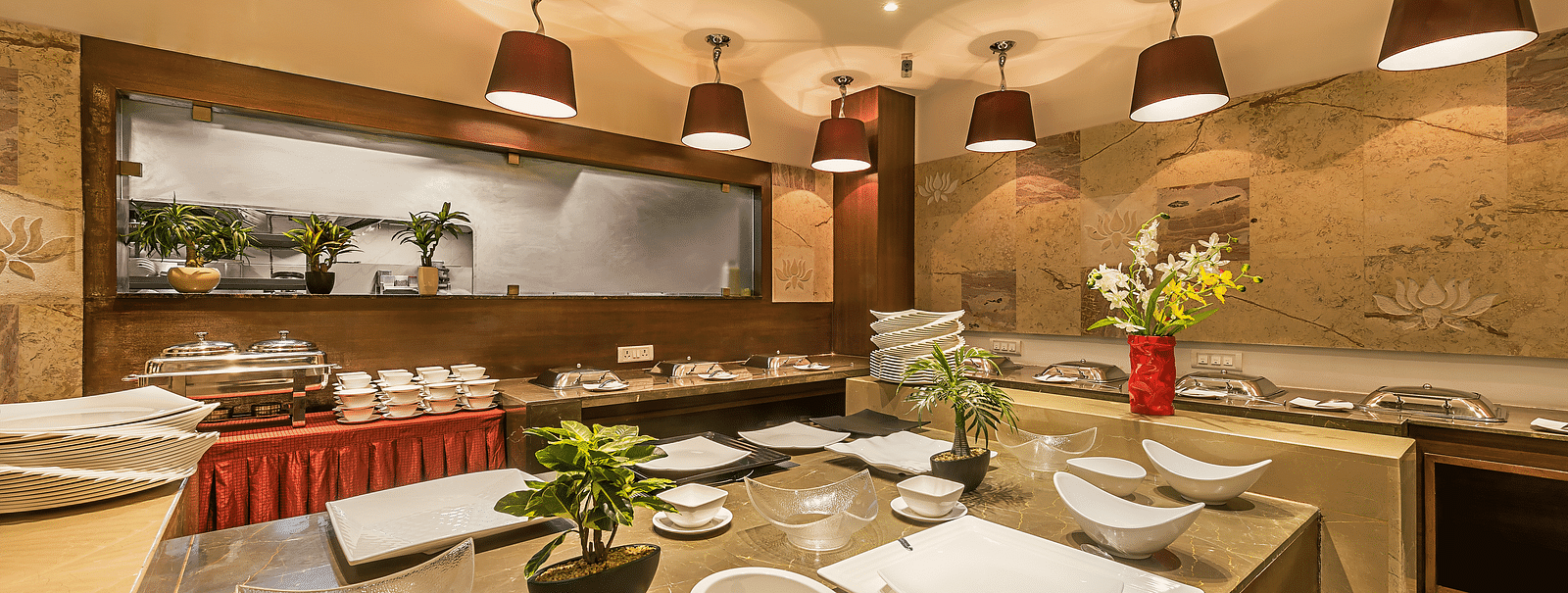 Elegant buffet area in a restaurant with wooden accents, red lampshades and a variety of white serving dishes arranged for use - TGI Grand Fortuna, Hosur