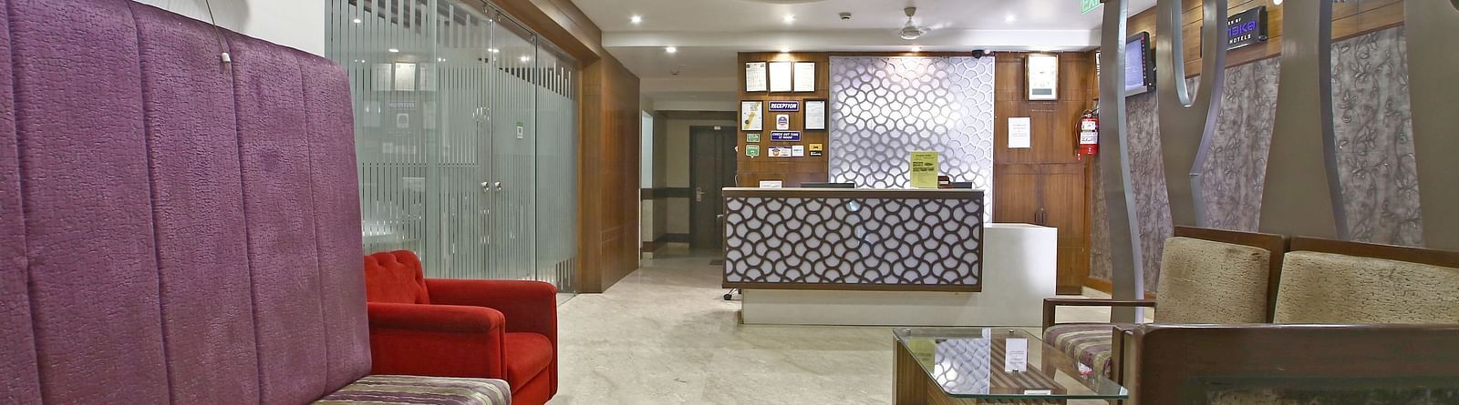 Seating area with modern ceiling design, bright lighting, a brown sofa on the right and a seating space on the left along with a red single chair and a reception desk in the far - Hotel Emerald, Chandigarh
