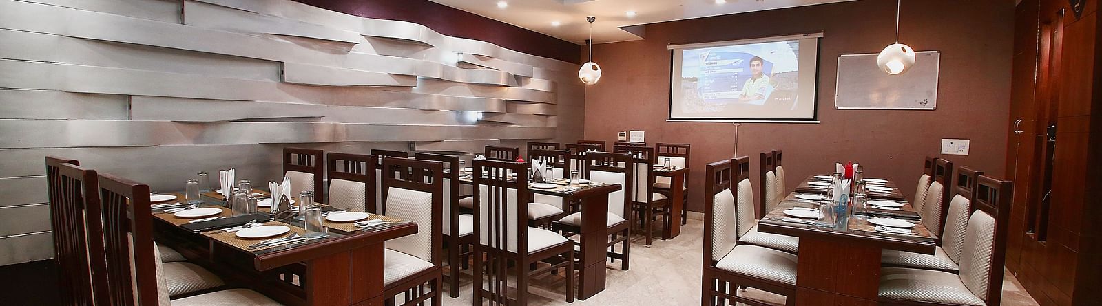 Modern dining space with various tables and chairs for guests to sit in and dine along with beautiful textured patterns on the wall and ambient  lighting - Hotel Emerald, Chandigarh