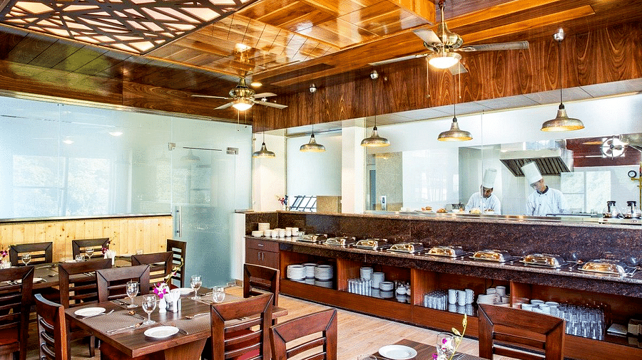 The restaurant at Regenta Inn DLS featuring the kitchen separated by a glass partition with a buffet counter in front of it.