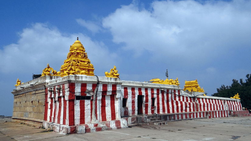 A temple structure with striped exterior walls, golden towers, and an open paved area in front.