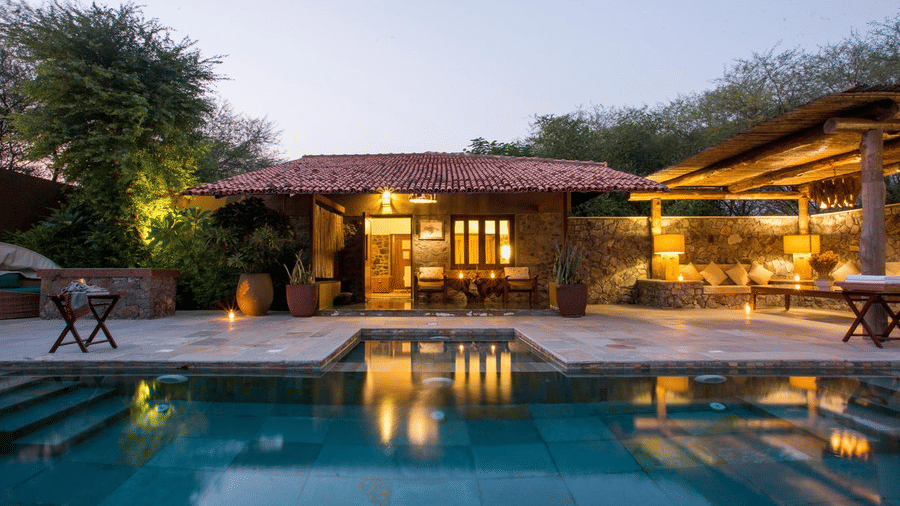Outdoor area of The Blackbuck Lodge, Velavadar featuring a swimming pool, villa, and lighting at dusk.