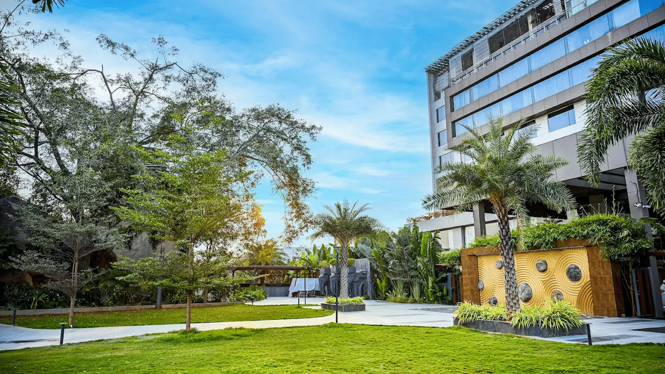 A modern multi-storey building of Daspalla Hotels beside a landscaped lawn with palm trees and paved walkways under a clear sky.