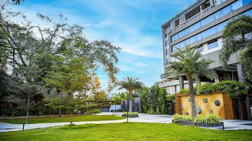 A modern multi-storey building of Daspalla Hotels beside a landscaped lawn with palm trees and paved walkways under a clear sky.