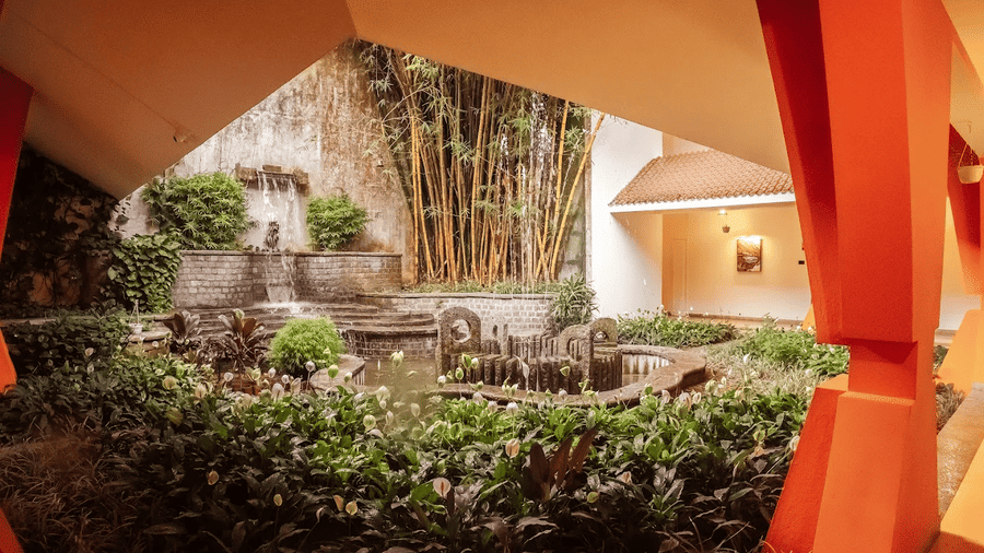 An outdoor view shows a walkway with plants, a structure, and stone elements at DNC Shevaroys Resorts and Spa.