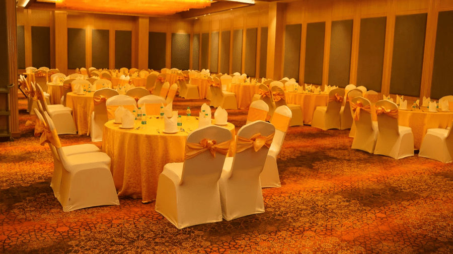 Indoor banquet hall set up for an event, with round tables, covered chairs, and a formal arrangement at Ramada Encore by Wyndham Chandigarh Zirakpur.
