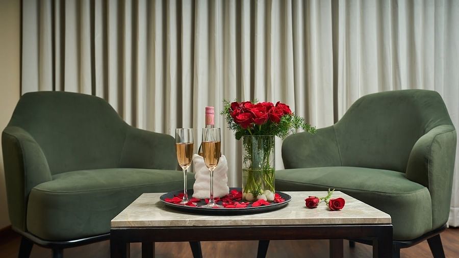 Two green coloured single sofas with a table with roses and wine on it in at Visthara - Urban Boutique Hotel, Bangalore
