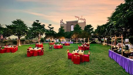 An outdoor area is prepared for an event with tables covered in red cloths on the grass - Lion Lords Inn Rajula