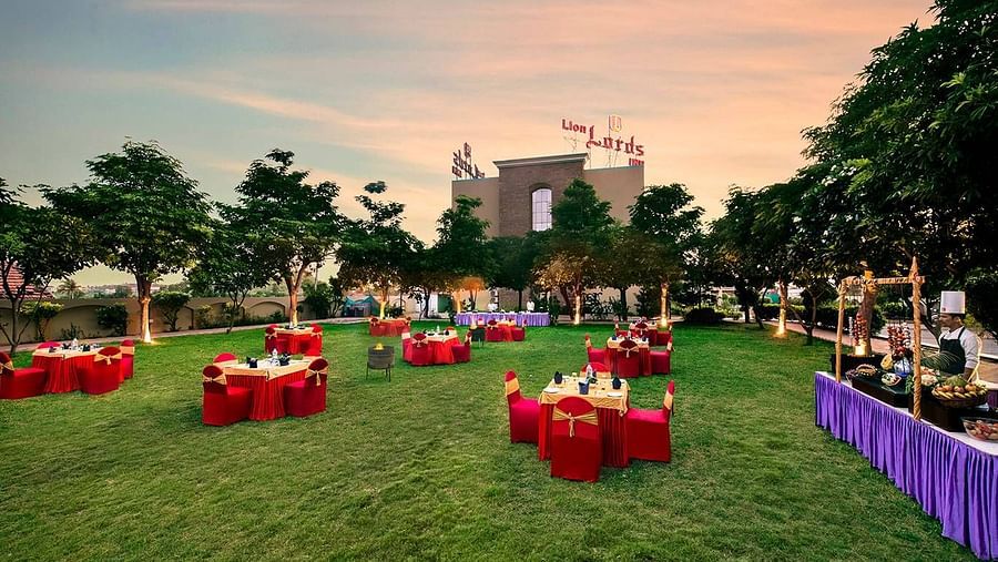 An outdoor area is prepared for an event with tables covered in red cloths on the grass - Lion Lords Inn Rajula