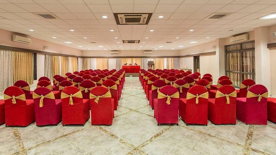 A large hall is set up with rows of chairs covered in red fabric for an event - Lion Lords Inn Rajula