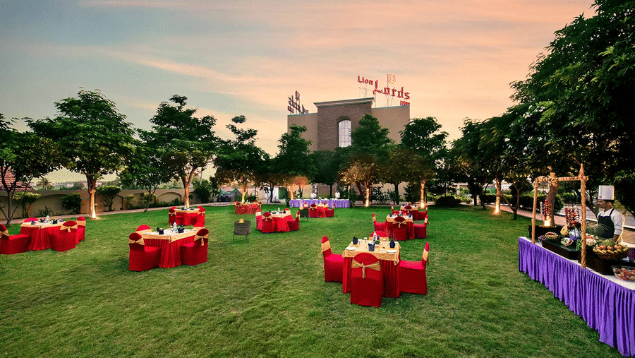 An outdoor area is prepared for an event with tables covered in red cloths on the grass - Lion Lords Inn Rajula