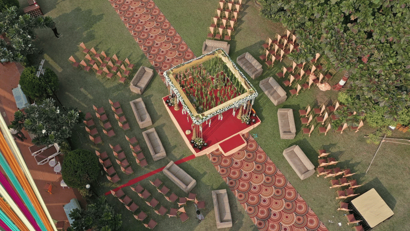 An aerial view of lawn area decorated for a wedding at VITS Kamats Resort, Silvassa, one of the best wedding resort in Silvassa with a carpeted pathway leading towards the main stage, and chairs and sofas kept facing the stage.