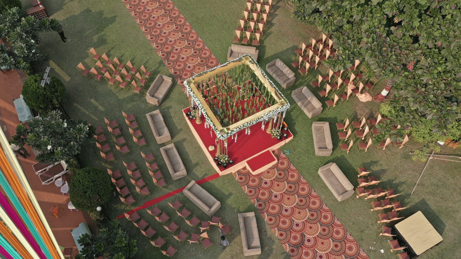 An aerial view of lawn area decorated for a wedding at VITS Kamats Resort, Silvassa, one of the best wedding resorts in Silvassa with a carpeted pathway leading towards the main stage, and chairs and sofas kept facing the stage.