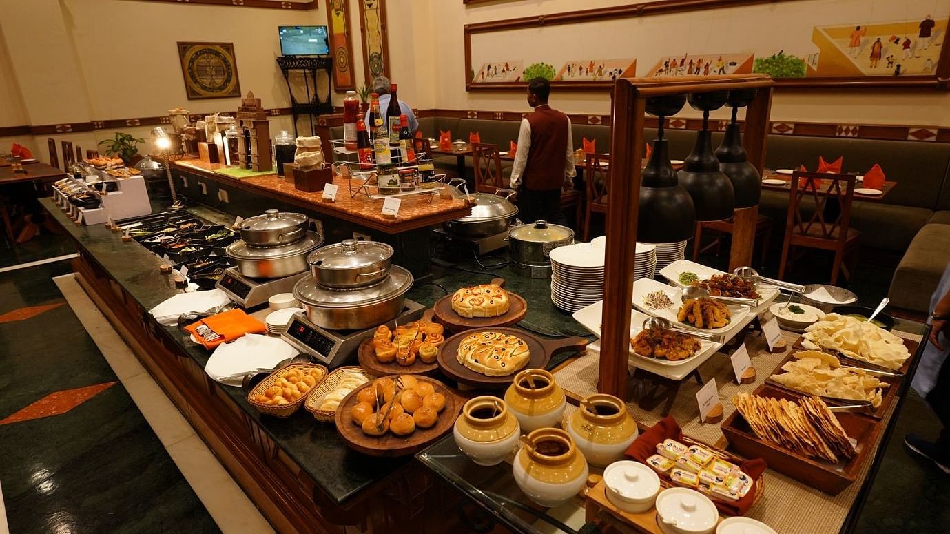 A lavish buffet spread featuring a variety of dishes including pastries, breads, and desserts is displayed on a long table in a warmly-lit, elegantly decorated dining area.