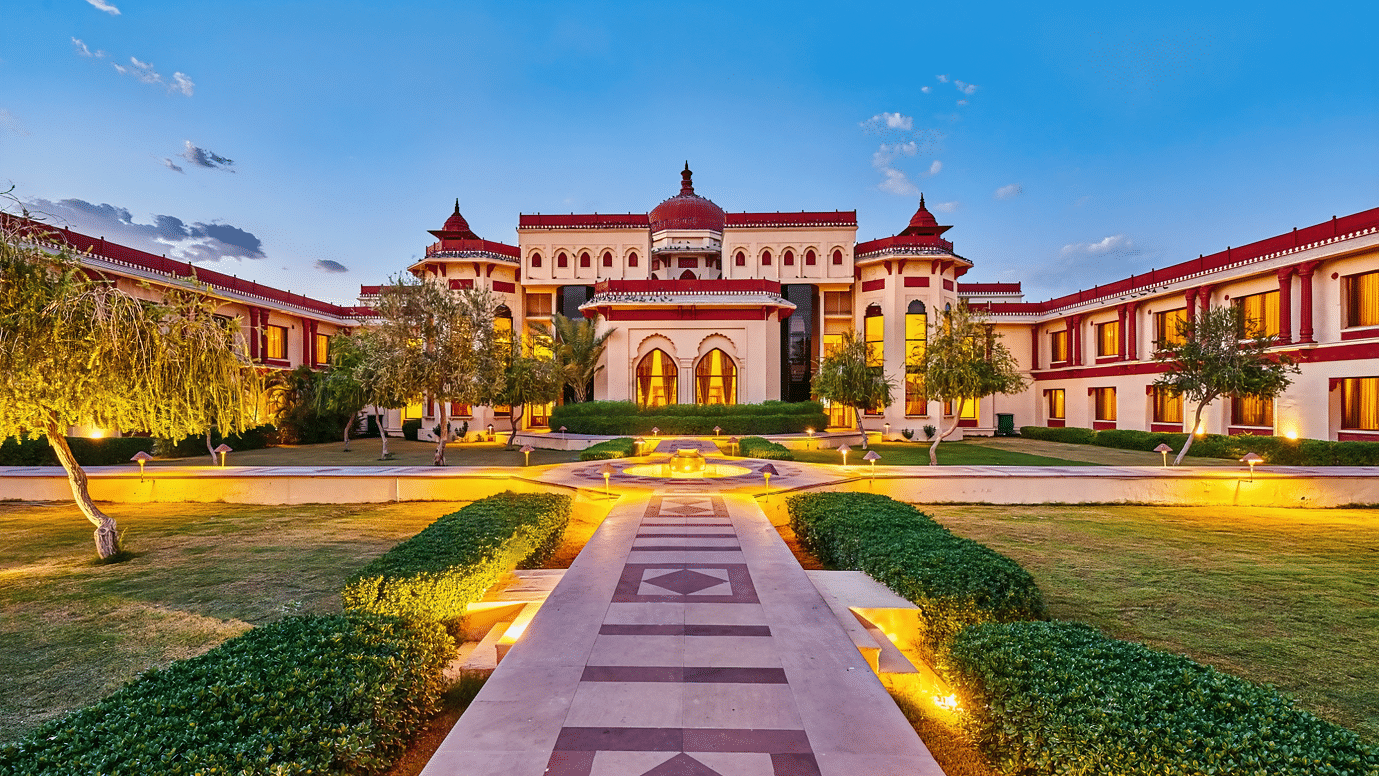 Wide-angle view of The Ummed Jodhpur facade in the evening, with lights glowing and the surrounding gardens enhancing the Palace Resort and Spa’s grandeur.