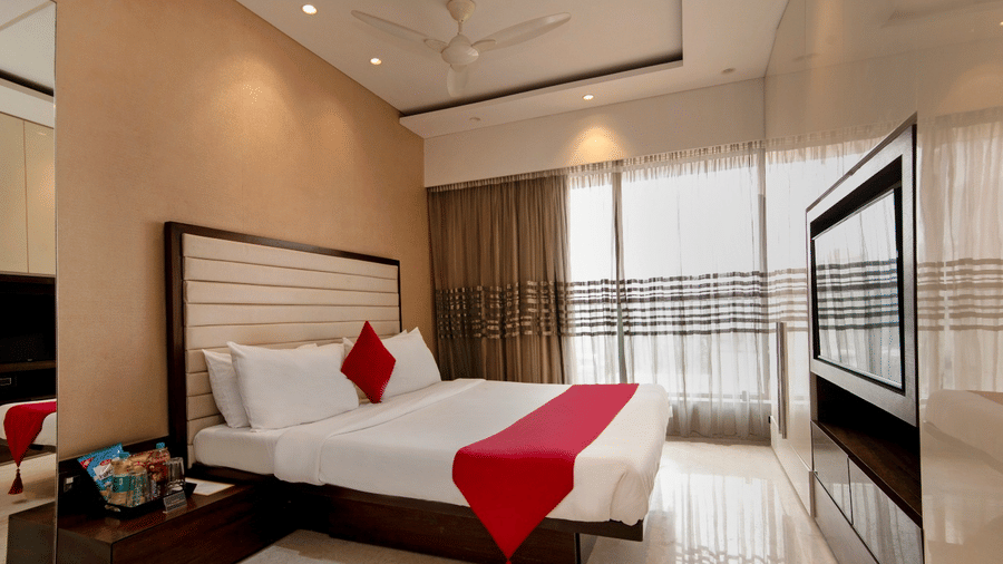 Modern bedroom at Theory9 - Premium Serviced Apts, Khar, with a padded headboard, red accent pillow, and large window for natural light.