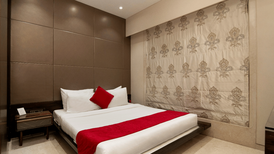 A bedroom at Theory9 - Premium Serviced Apts, Khar, featuring a brown paneled accent wall and patterned window shade.