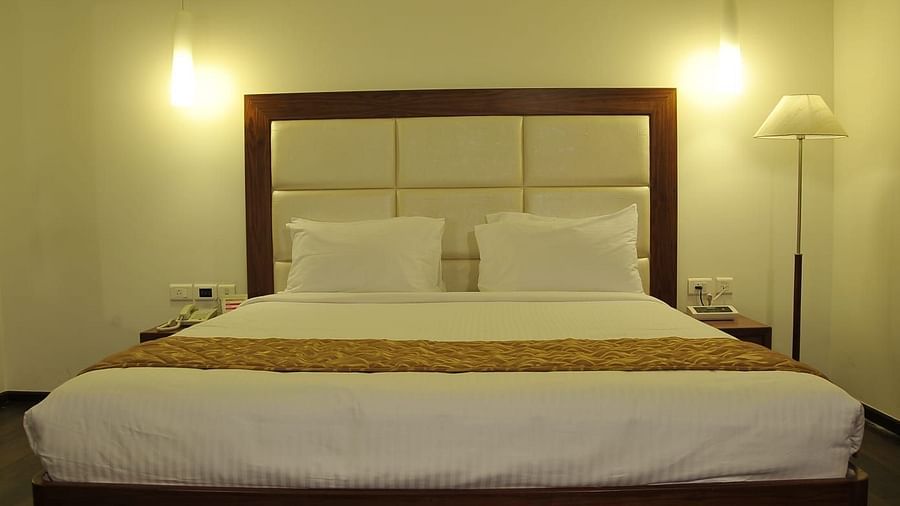 Close up of Suite at Dhanalakshmi Srinivasan Hotels, Perambalur featuring kind bed, furniture, and warm lighting. 