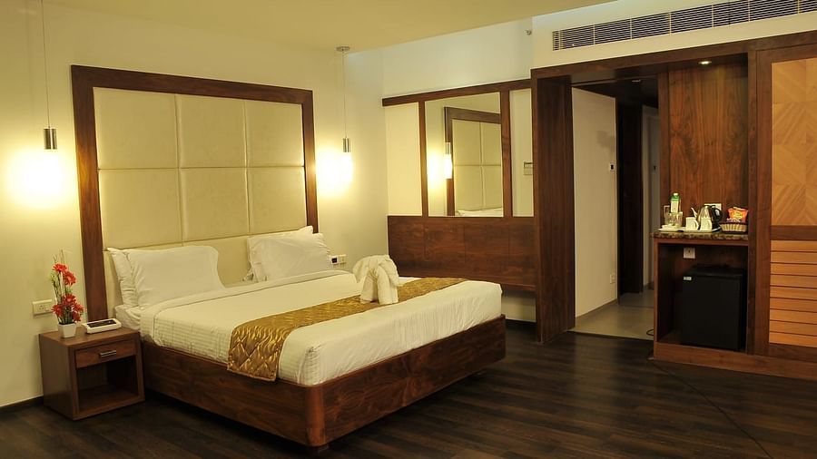 A Executive Suite at Dhanalakshmi Srinivasan Hotels, Perambalur featuring a bed with white linens, dark wood flooring, and a mini-fridge.