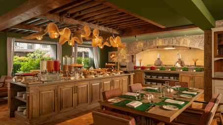 A wide-angle shot of Mila Restaurant at The Evren, Vagator, featuring a buffet counter in the middle of the dining area surrounded with well-arranged tables with cutlery and napkins.