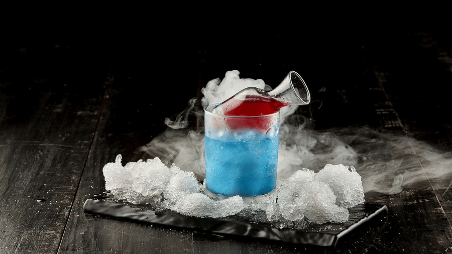 Signature blue cocktail at The Citrine, Bangalore, with smoking dry ice, and a red liquid pour from a jigger on a slate platter with ice.