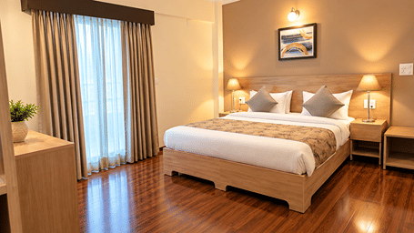 Deluxe One Bedroom Suite at Starlit Suites, Shirdi, with a large bed, patterned runner, bedside lamps, framed artwork, curtains and glossy wooden flooring.