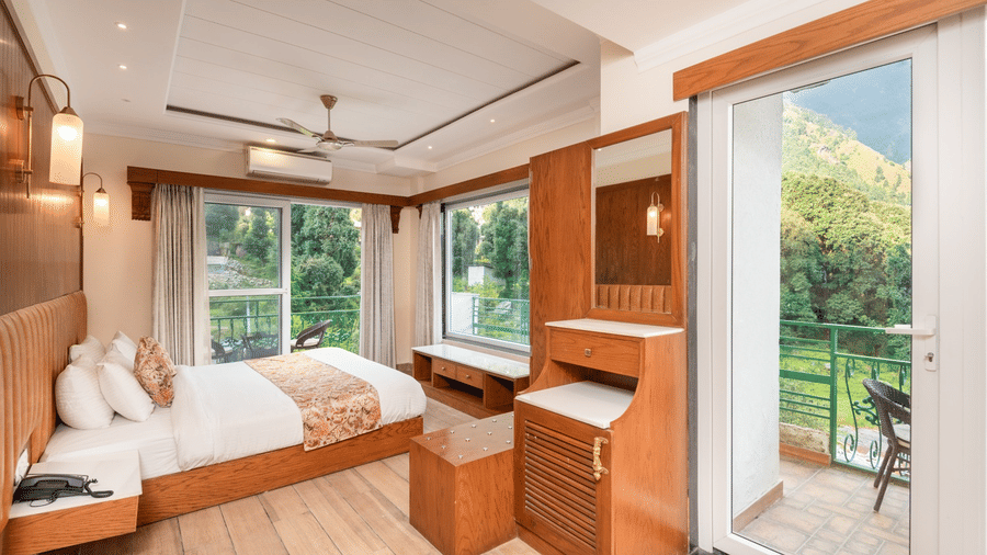 A spacious family suite at Quality Inn with a king size bed, a dressing table, and a balcony with a scenic view.