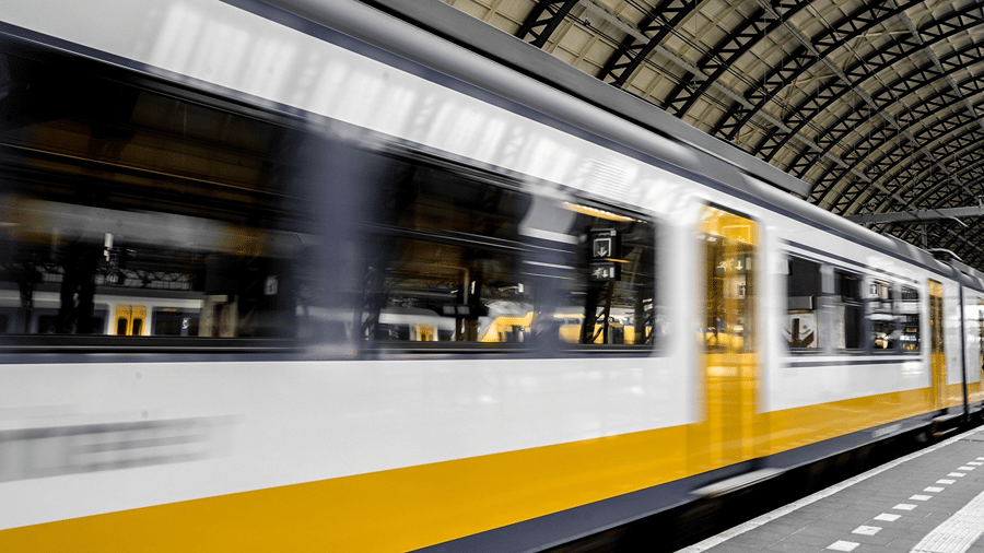 A high-speed train with yellow stripes passing under a station roof