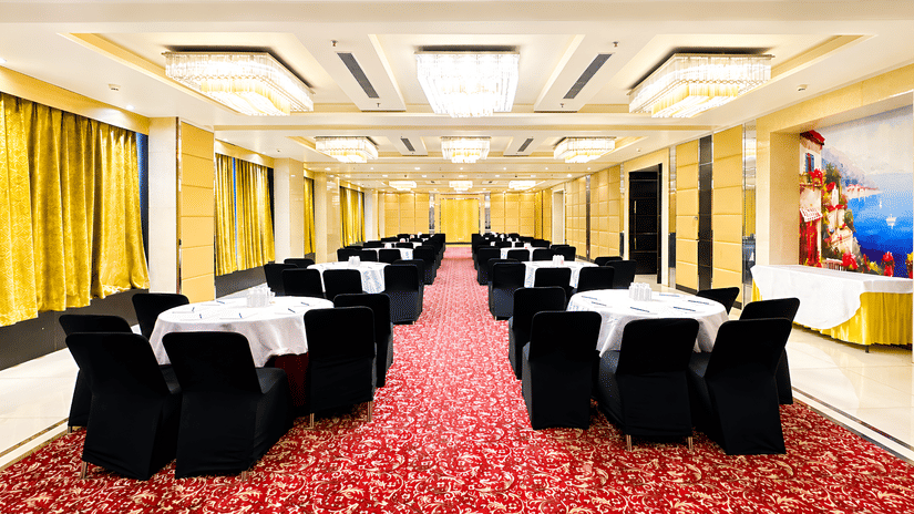 Reception area at Golden Tulip Kukas Jaipur featuring a white front desk, ornate dark patterned wall, marble floors, and warm overhead lighting.