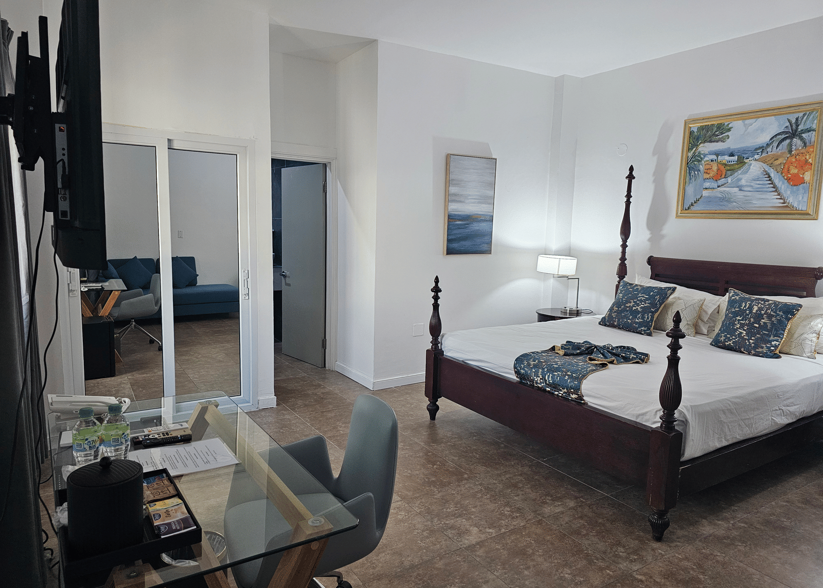 The Junior King Suite at Hotel 39, Jamaica, with a 4-poster bed, a glass-top work desk, a wardrobe, and an open bathroom doorway.