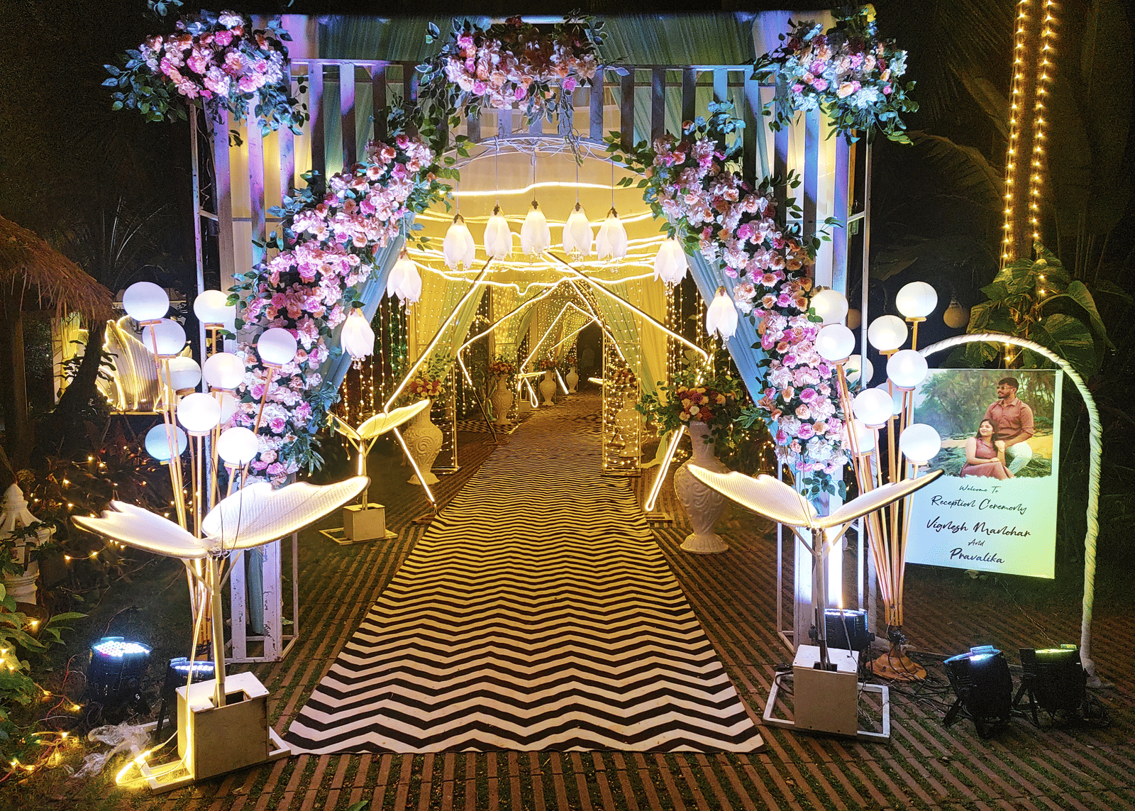 Entrance arch decorated with pink and white flowers and lights at Paradise Lagoon Resort, Udupi.