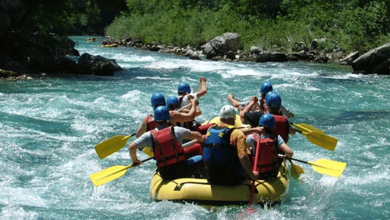 A group of people wearing life jackets and helmets paddling a yellow raft through whitewater rapids on a river.