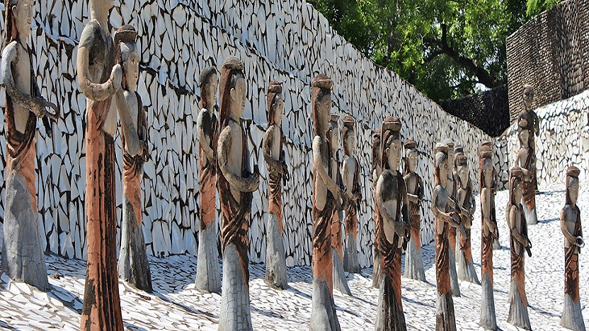 Row of wooden figure sculptures set against a stone wall.