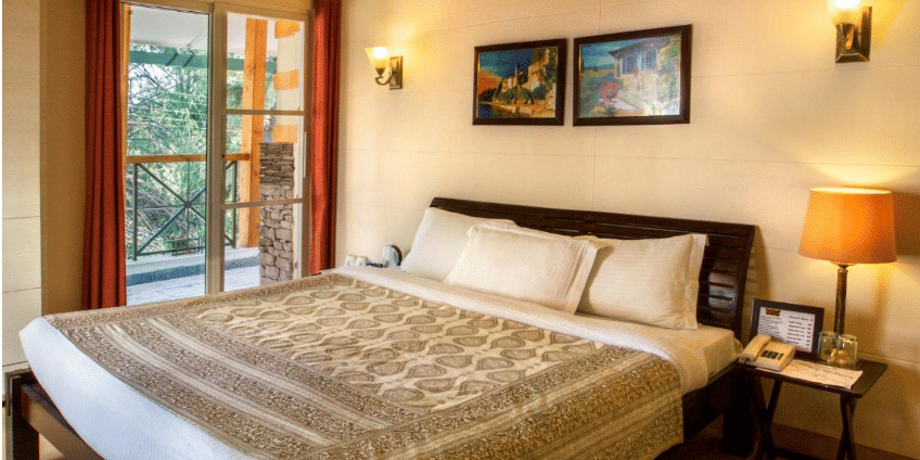 Deluxe room designed with aesthetic interior with  beautiful shades of brown while showcasing a beautiful balcony beside the bed - Lamrin Norwood Green, Palampur