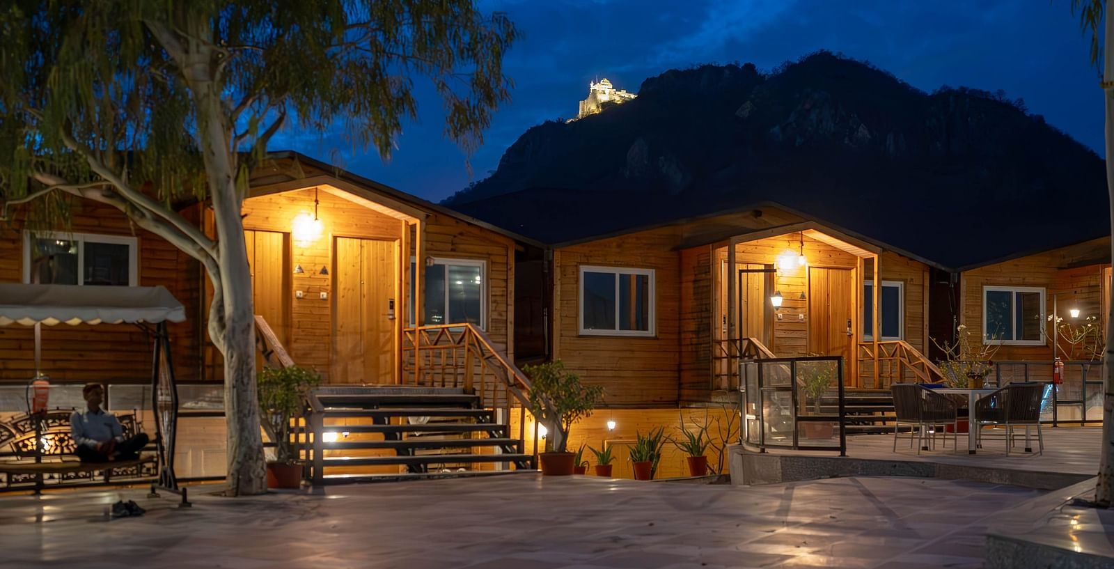 A facade of Bamboo Saa Resort & Spa, Udaipur with warm lights at night and the background shows a mountain or hill.