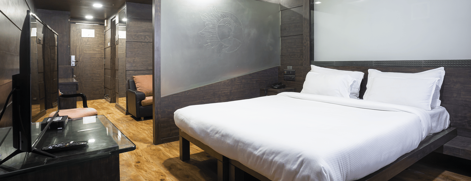Bedroom with a king size bed, side table and dark wall panels at Infiniti Hotel, Indore.