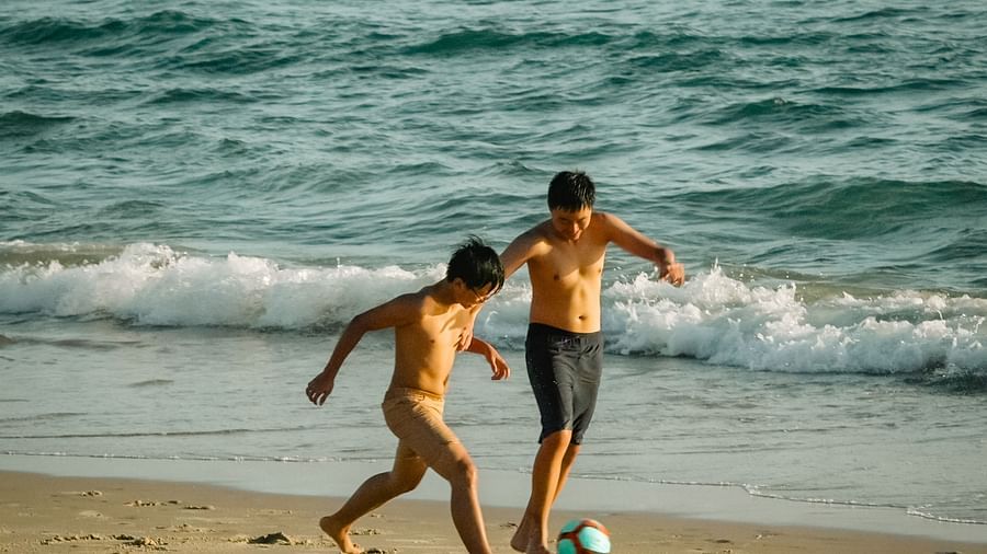 Two kids playing football on the beach