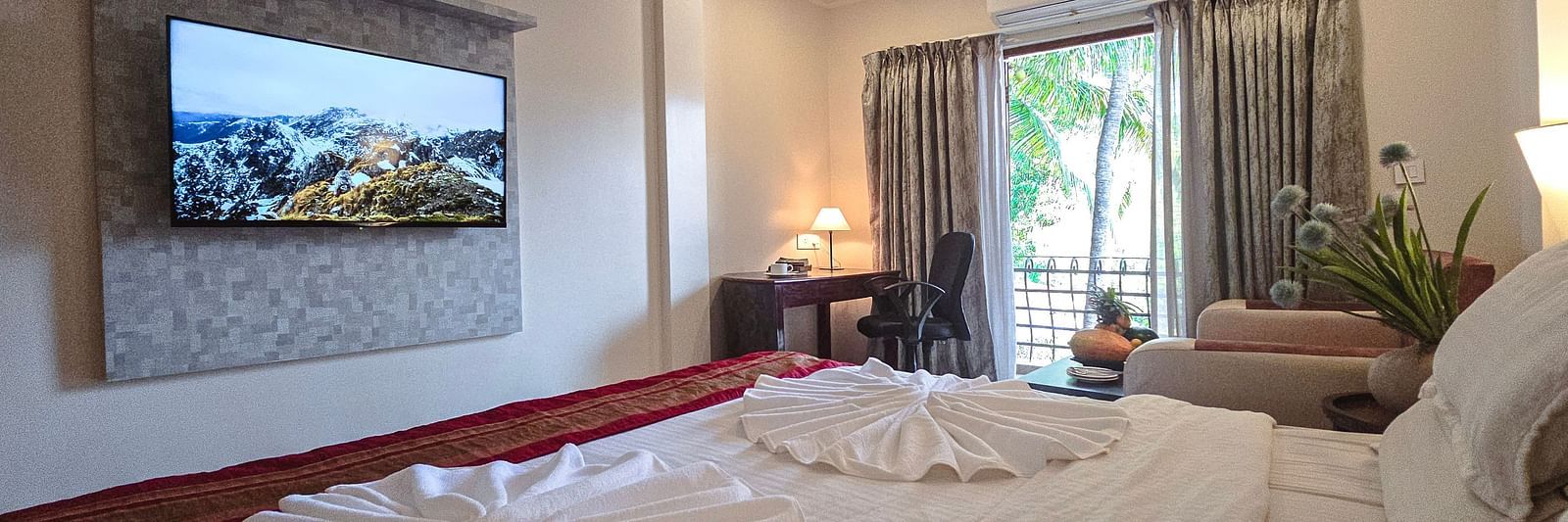 A spacious bedroom with a bed, towel art, and a wall-mounted flat-screen TV – The Verda de Miranda Resort.