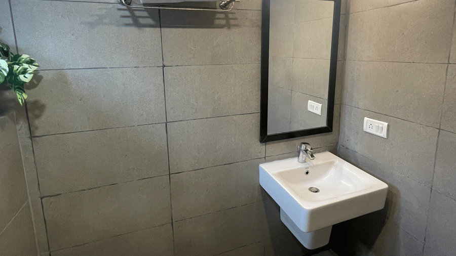 Sanctum Suites, Richmond Road, Bangalore features a tiled bathroom with a white washbasin, a rectangular mirror with a light, and a metal towel rack.