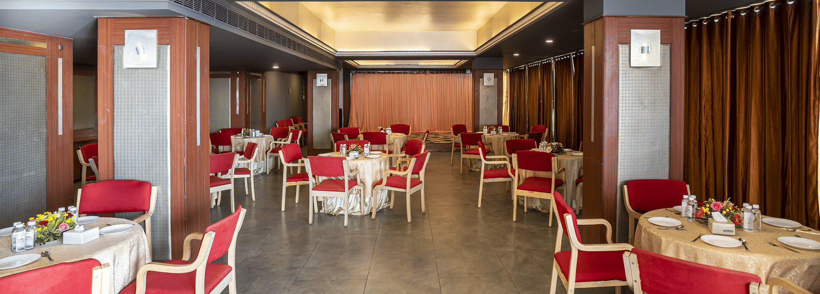 A dining hall with red chairs, white tables and warm ceiling lights at Infiniti Hotel, Indore.