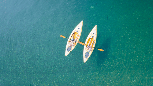 Two kayaks with people paddling on clear waters.