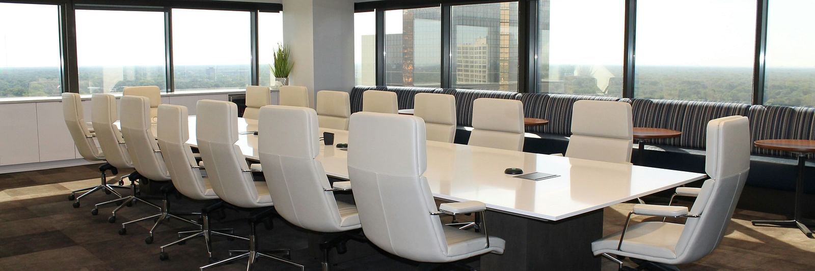 A modern conference room with a long table, white chairs, and large windows overlooking a city view.