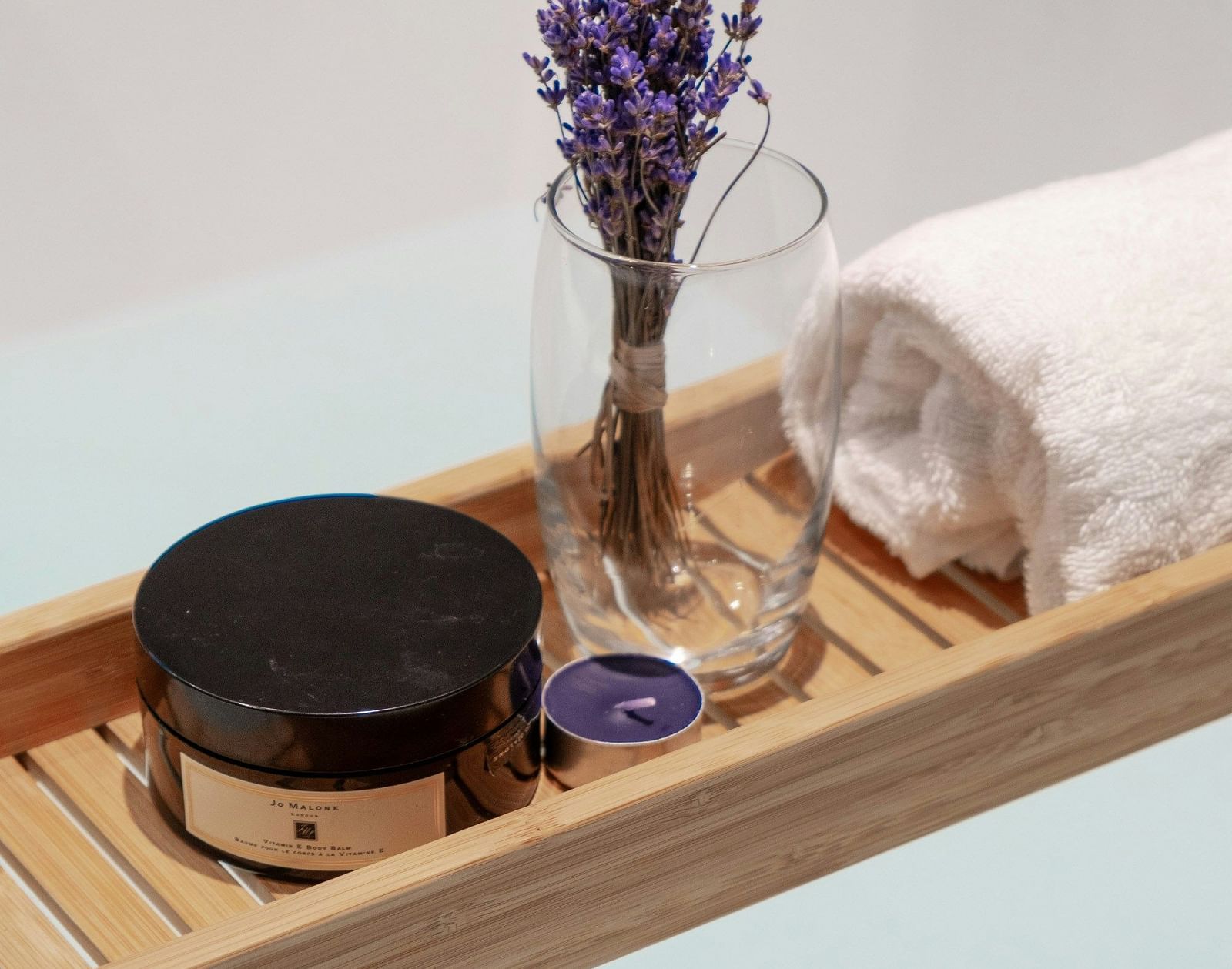 A bathtub with a wooden tray holding bath products, including lavender, and towels.