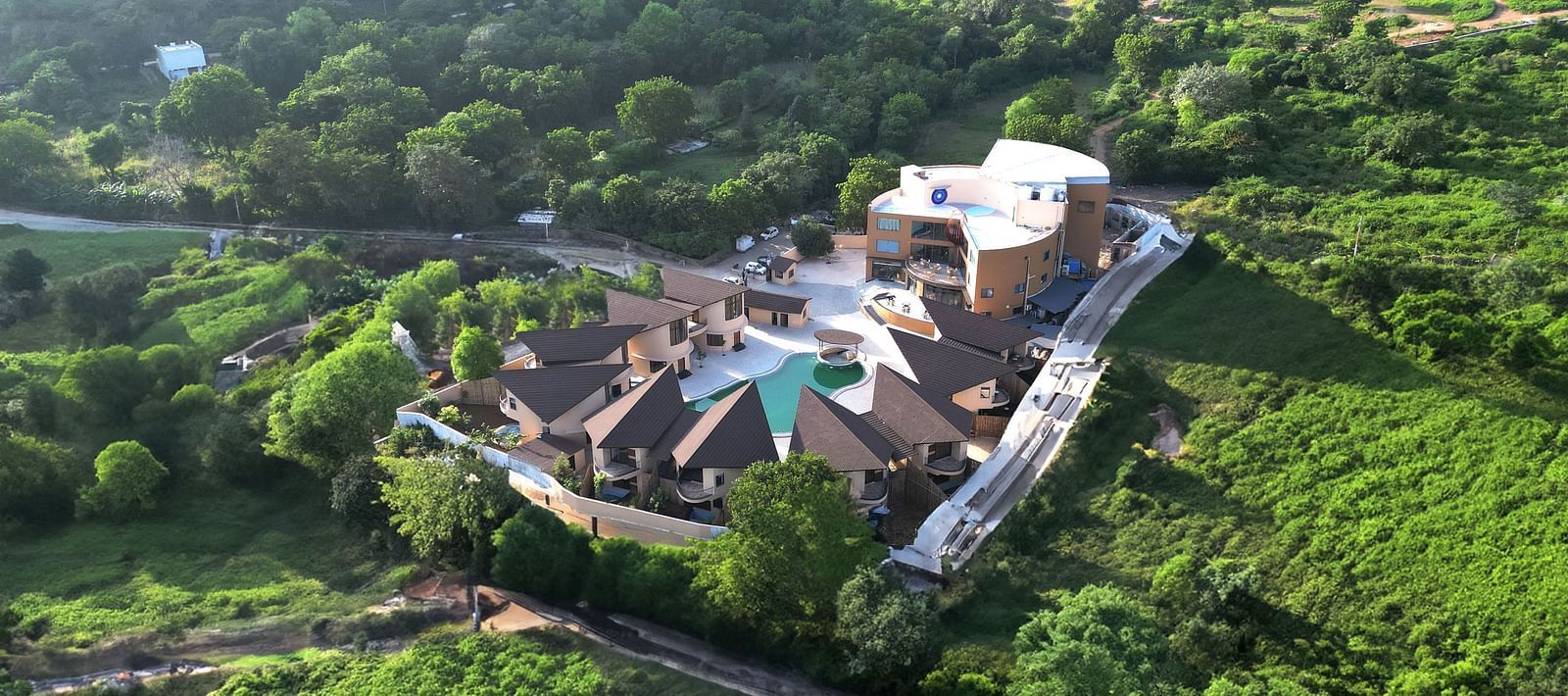 An aerial view of The Qualia Resort Club & Brewery, Udaipur surrounded by lush greenery and hills.