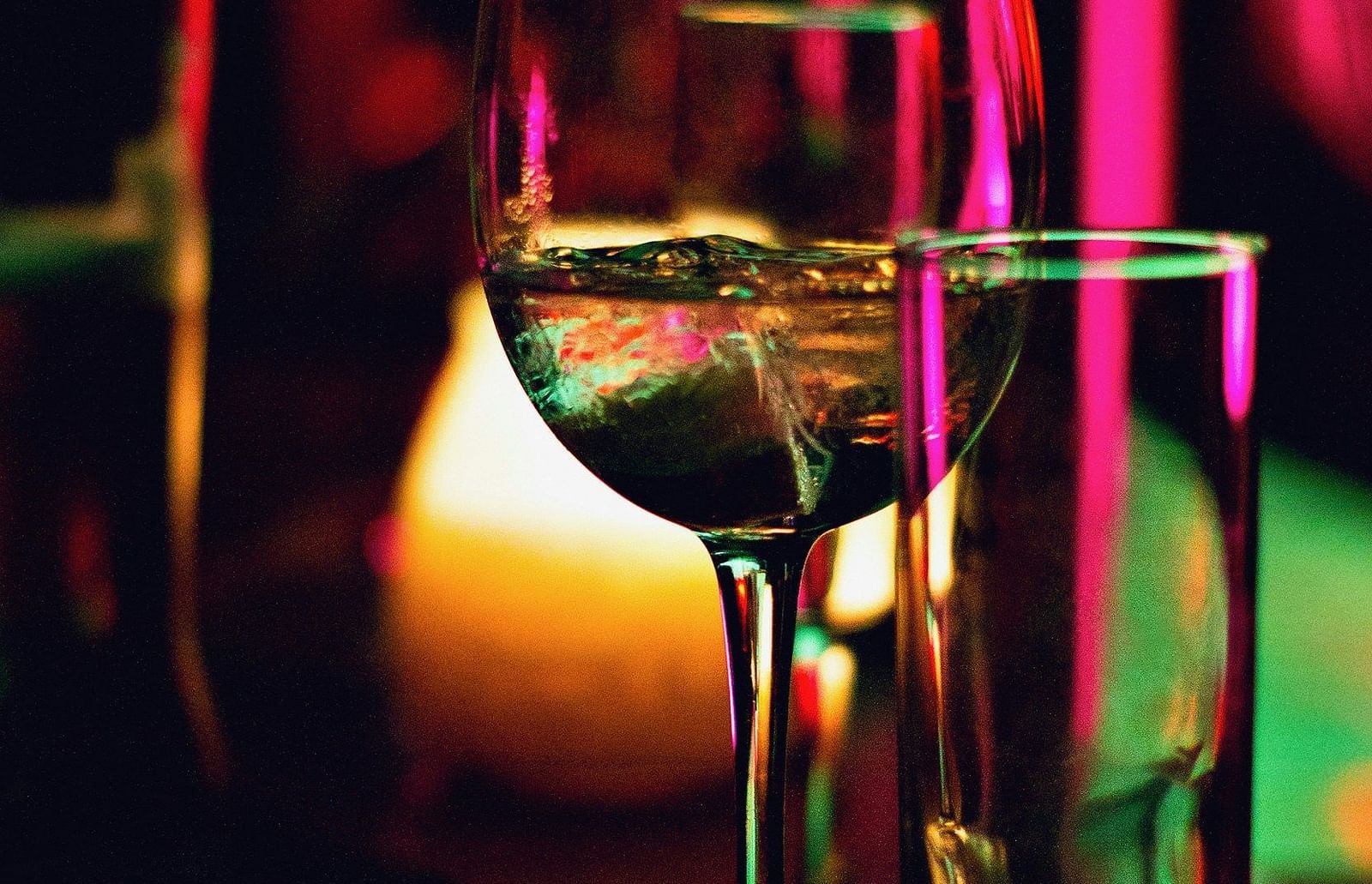 Two glasses, one with ice, glowing under the coloured bar lights.