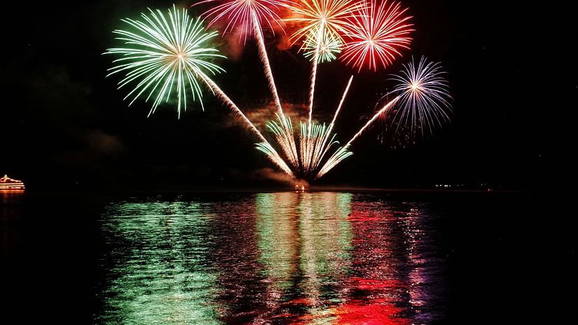 A far out view of fireworks in the distance on the sky with its reflection on the waterbody in view