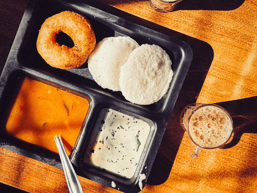 A plate with south indian breakfast along with filter cofee on the side.