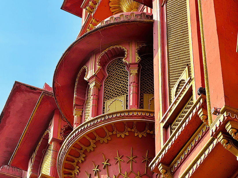 A building facade with red exterior walls, balconies, windows, and decorative architectural details against the sky.
