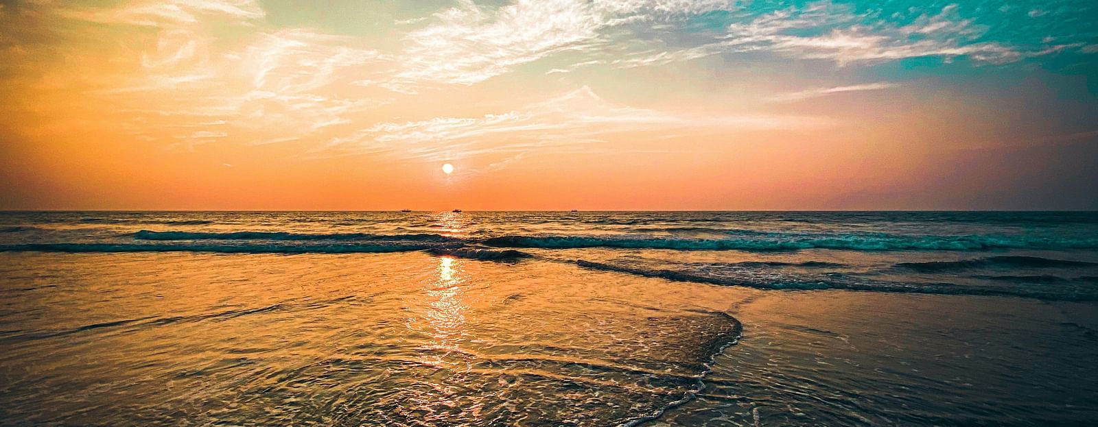 an overview of a beach in goa with the sun setting while creating different hues in the sky.